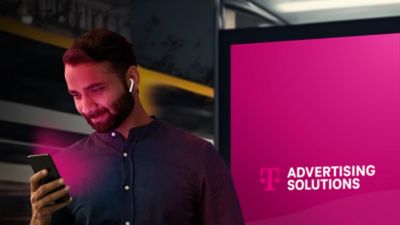 Hombre mirando un teléfono móvil, de pie delante de una pantalla digital al aire libre con la frase "T-Mobile Advertising Solutions".