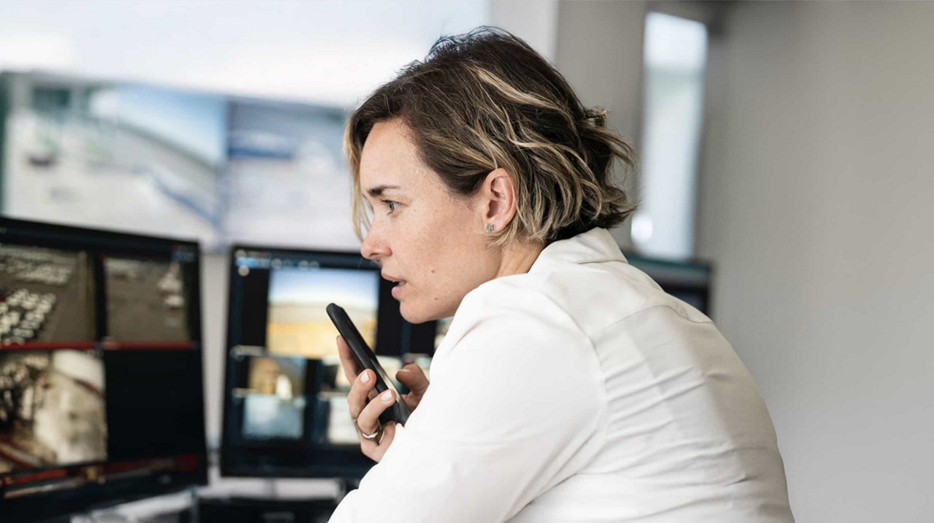 Un profesional utiliza la bocina de un teléfono móvil desde una estación de trabajo con varios monitores.