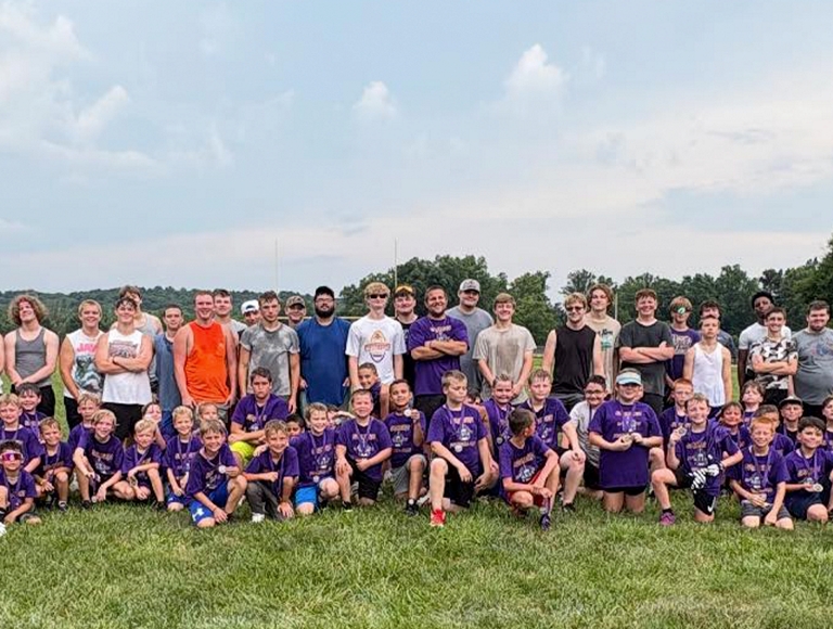 El equipo de fútbol americano de Eastern High School posa para una foto con un grupo de niños con camisetas moradas.