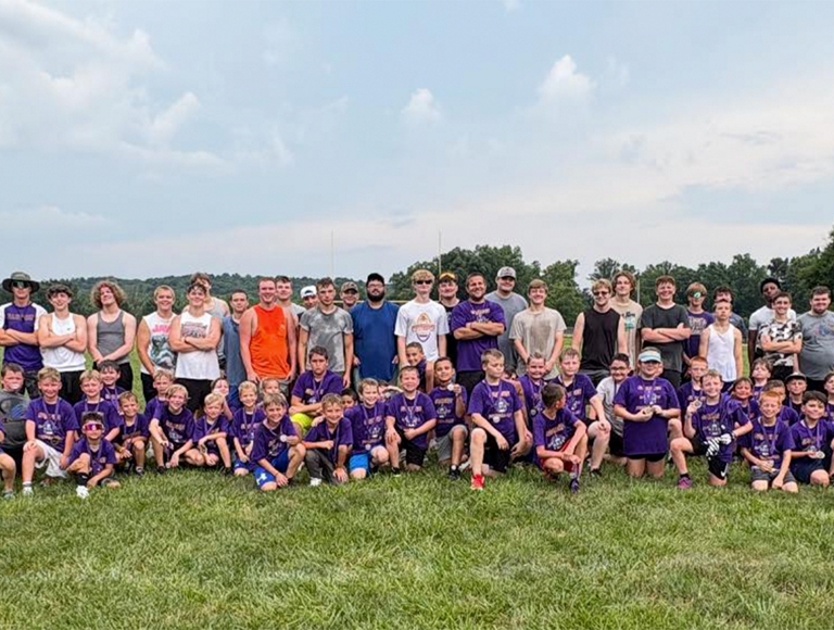 El equipo de fútbol americano de Eastern High School posa para una foto con un grupo de niños con camisetas moradas.