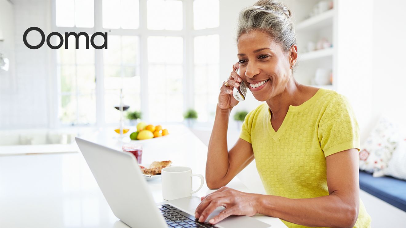 Ooma. Mujer sonríe y habla por teléfono de línea fija mientras está reclinada en una silla.