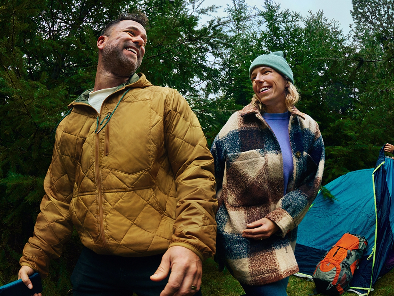 Un hombre con un teléfono sonríe a su amigo en un campamento.