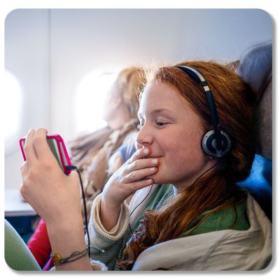 Una niña con audífonos sonríe a su teléfono al abordar un avión.