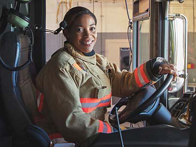 Una bombera sonríe sentada al volante de un camión de bomberos.