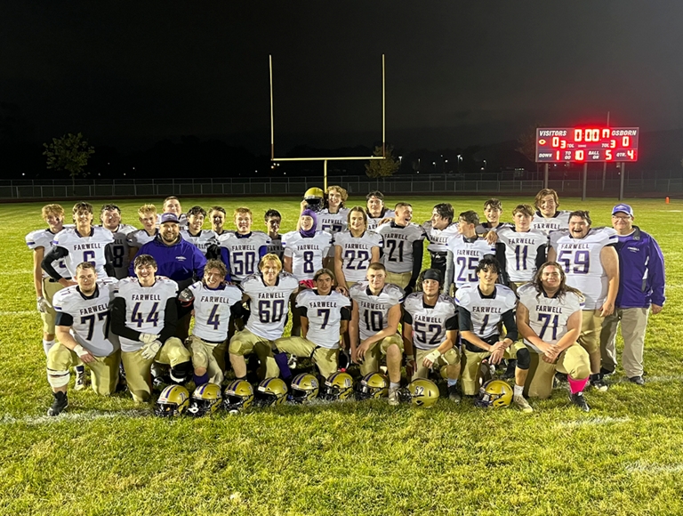 El equipo de fútbol de Farwell Area, con uniformes en dorado y morado, posa para una foto con el tablero de puntuación en el fondo.