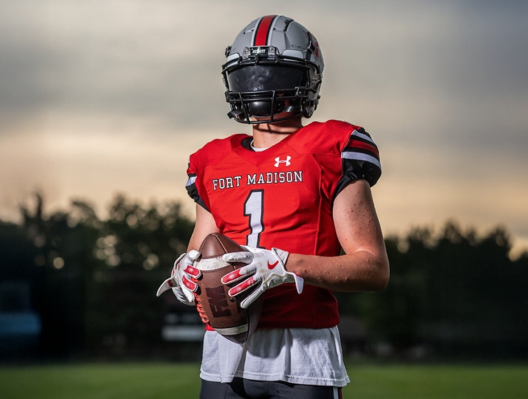 Un jugador de fútbol de Fort Madison sostiene un balón en el campo durante el crepúsculo.