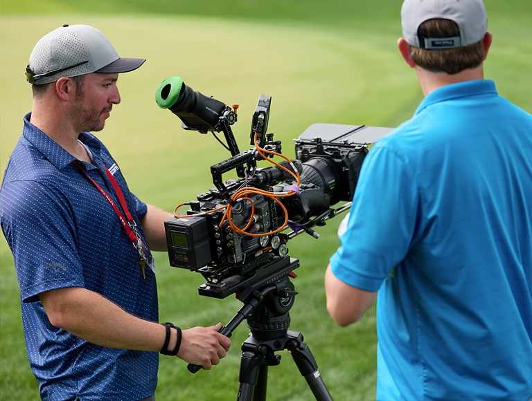 Dos miembros del personal operan una cámara en el campo de golf.