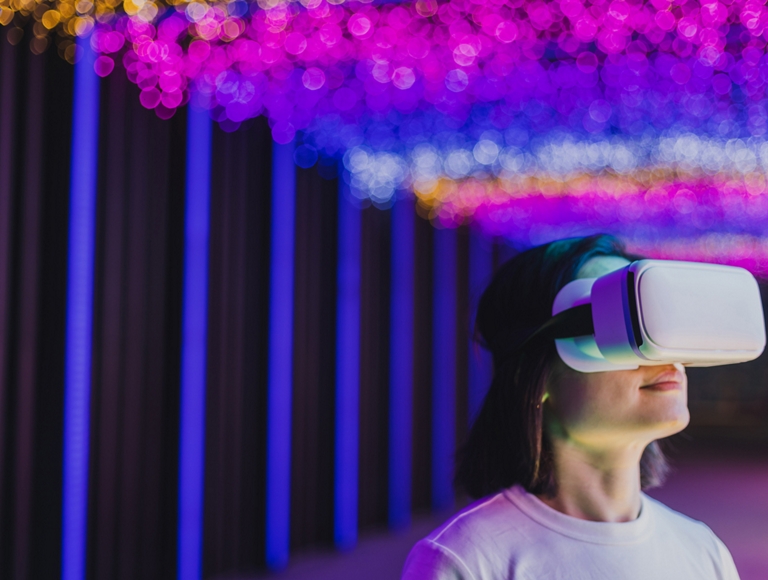 Una persona usa un casco de realidad virtual en una habitación iluminada con luces suaves y multicolores.