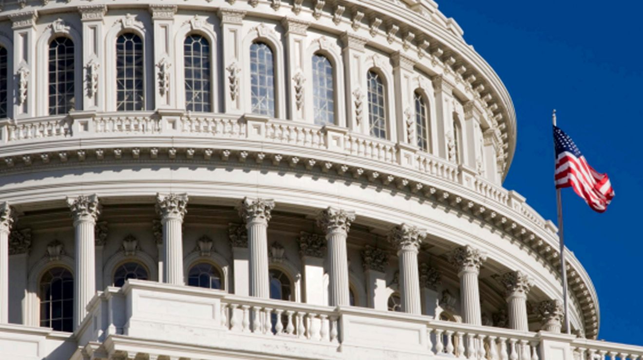 Primer plano de la cúpula del Capitolio de los Estados Unidos y la bandera estadounidense contra un cielo azul.