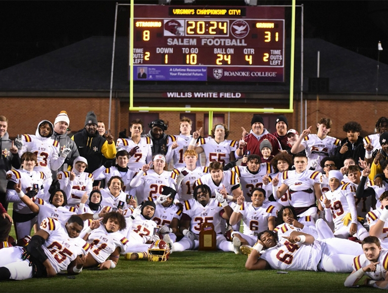El equipo de fútbol americano de Graham High School, con uniforme blanco, posa debajo del marcador en la zona de anotación.