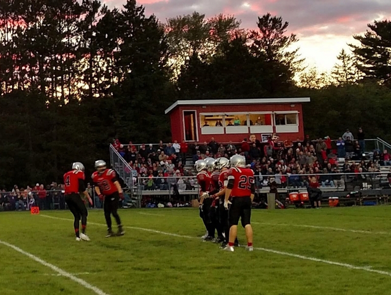 Jugadores de fútbol de Hinckley-Finlayson, vestidos con uniformes rojos y negros, toman sus posiciones en el campo.