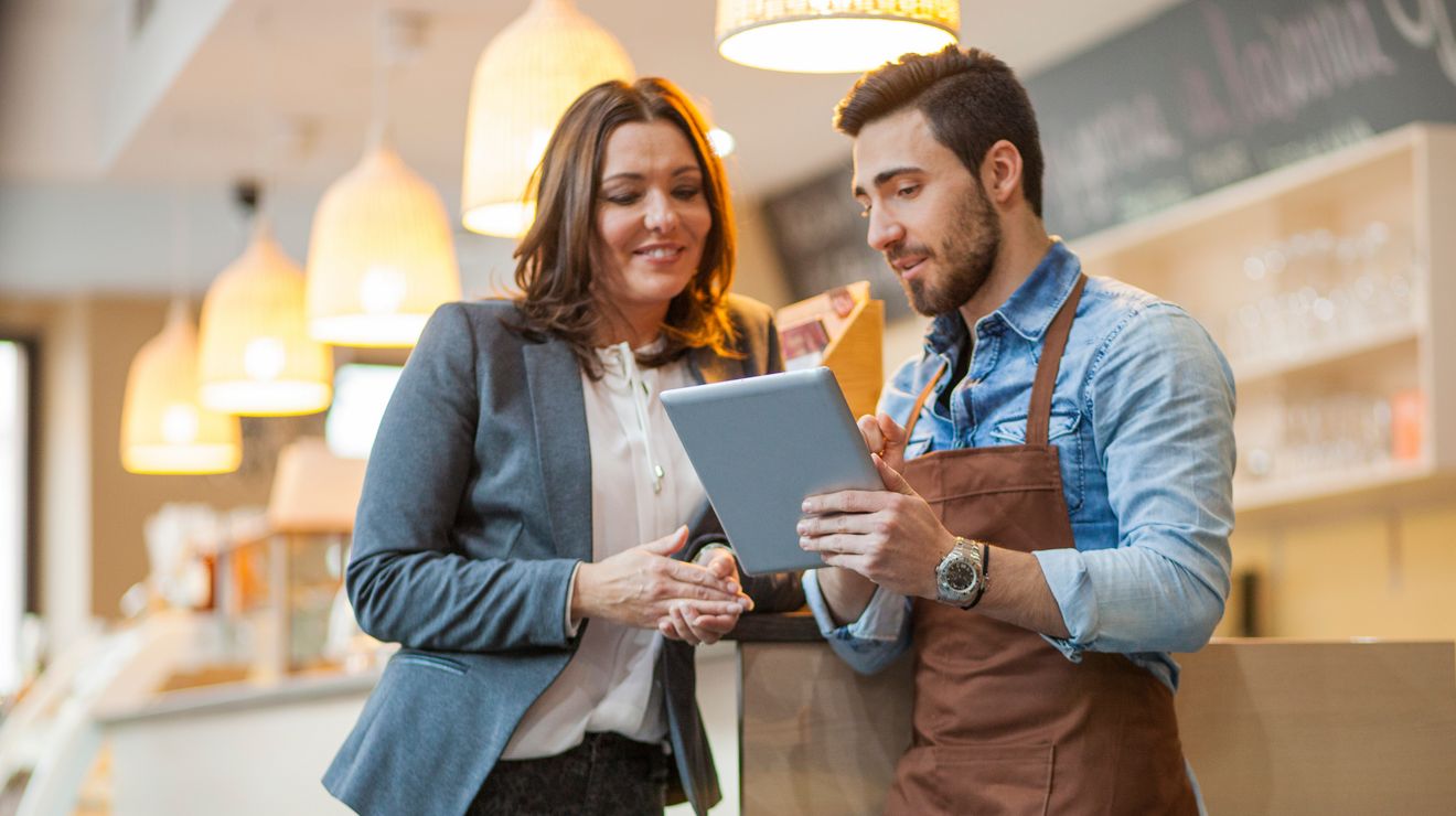 Una gerente y un barista utilizando una tablet para revisar las operaciones minoristas en una cafetería.