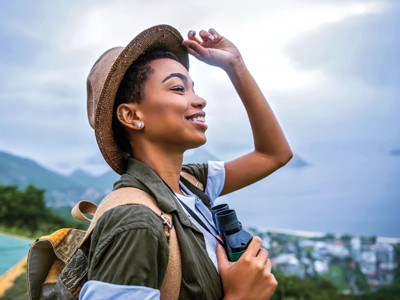 Mujer joven levantándose el sombrero para ver mejor, con un paisaje tropical de fondo