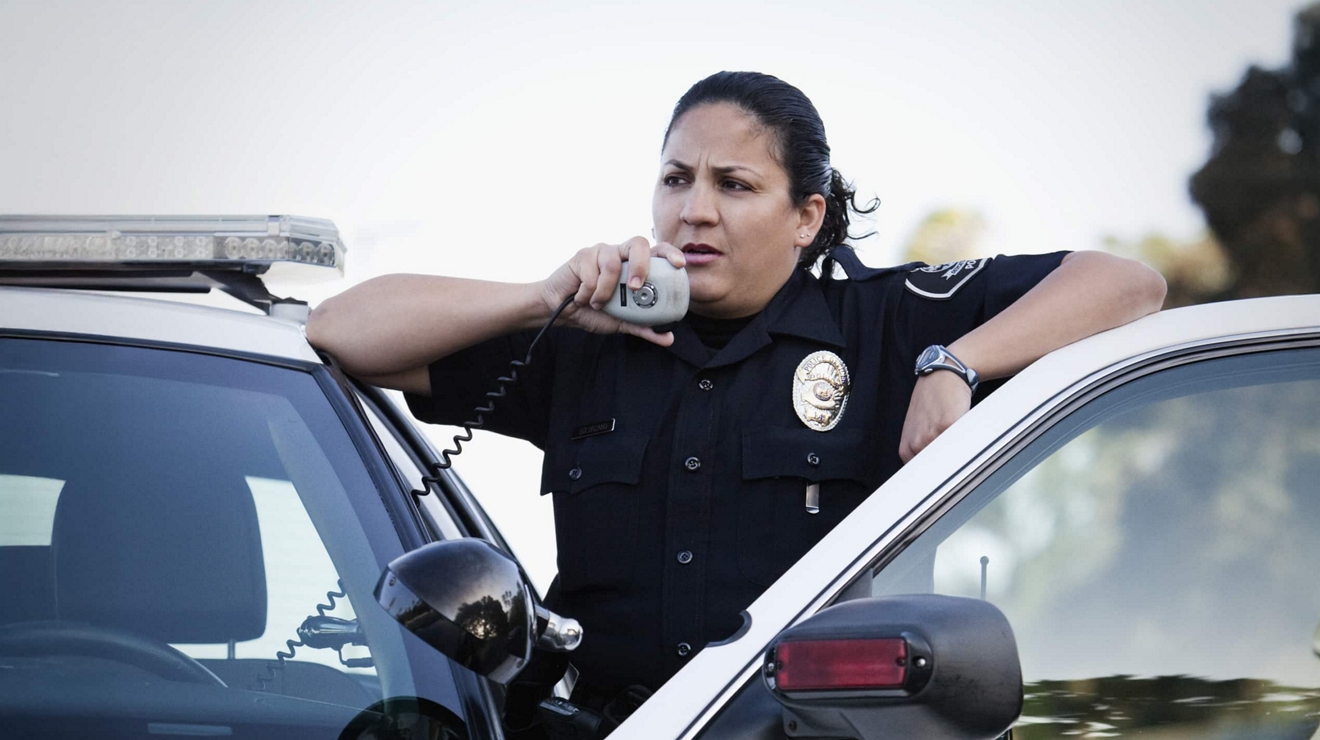 Miembro de servicios de emergencia en un vehículo patrulla utilizando un sistema de radio de interoperabilidad con LMR para comunicarse con sus compañeros.