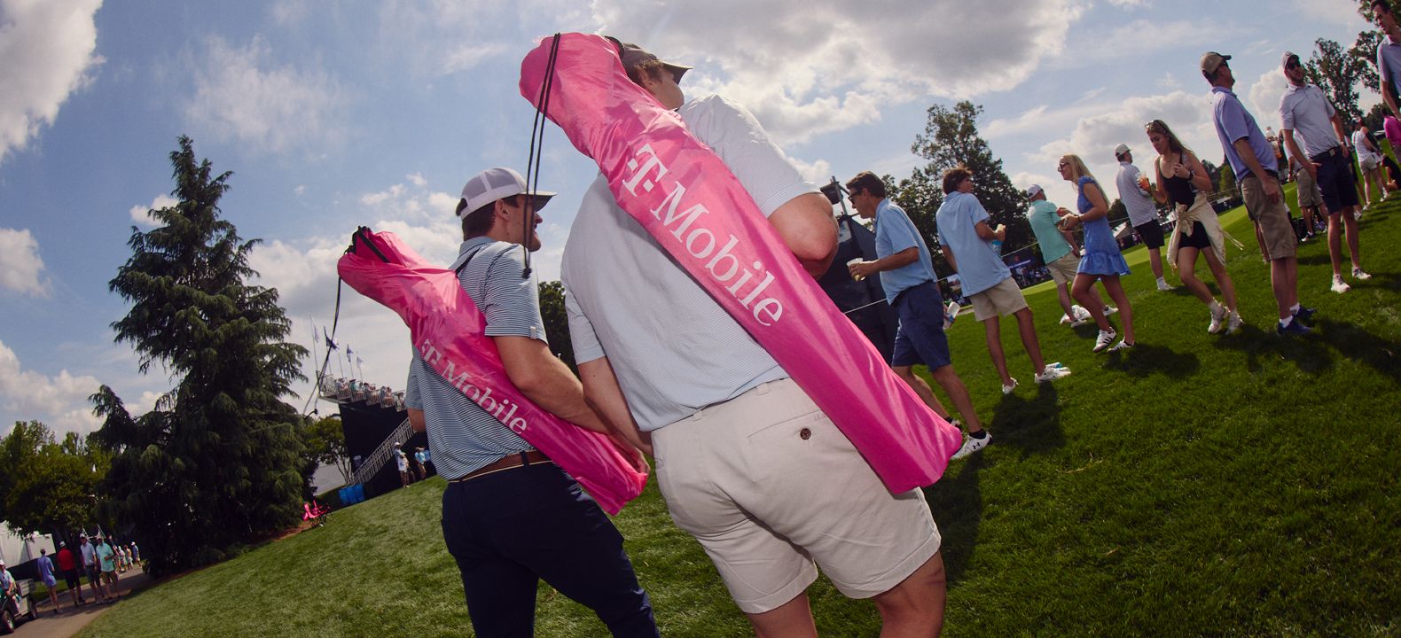 Dos miembros de T-Mobile llevando sillas de jardín al campo de golf.