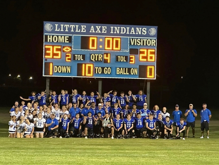 El equipo de fútbol americano y las animadoras de Little Axe High School posan para una foto debajo de su marcador.