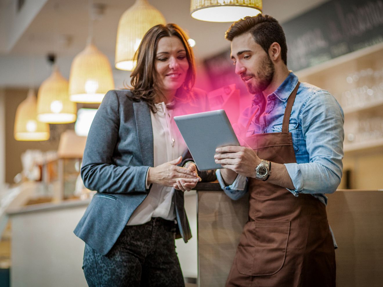 Un empleado en una tienda usa una laptop con un brillo magenta de T-Mobile para ayudar a un cliente.