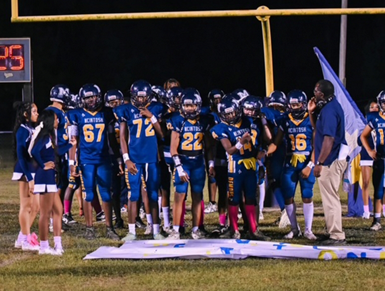Jugadores de fútbol y porristas de McIntosh High School se reúnen en el campo antes de un partido.