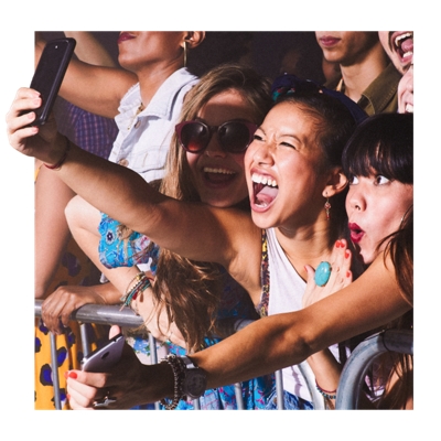 Un grupo de amigos en un concierto sosteniendo sus teléfonos, sonriendo y celebrando en la primera fila.
