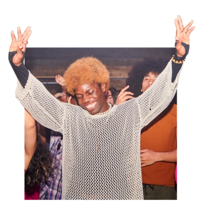 Una persona sonriendo mientras mira hacia abajo con las manos levantadas alegremente en medio de una multitud de gente en una fiesta.