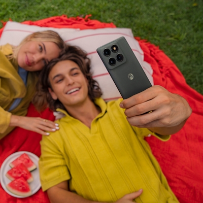 Dos amigos tumbados sobre una manta de picnic con comida, haciéndose un selfie con un moto edge.