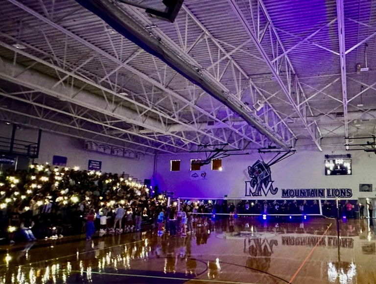 Alumnos de Mountain View sostienen luces brillantes en un gimnasio a oscuras.