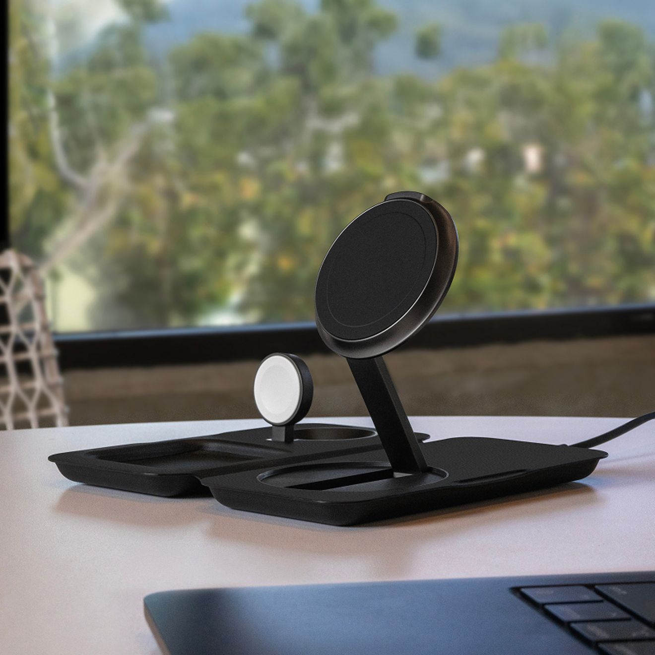Una estación de carga inalámbrica Nimble Fold 3 en 1 de color negro está desplegada sobre un escritorio, con zonas de carga específicas para un smartphone, un Apple Watch y unos audífonos inalámbricos.