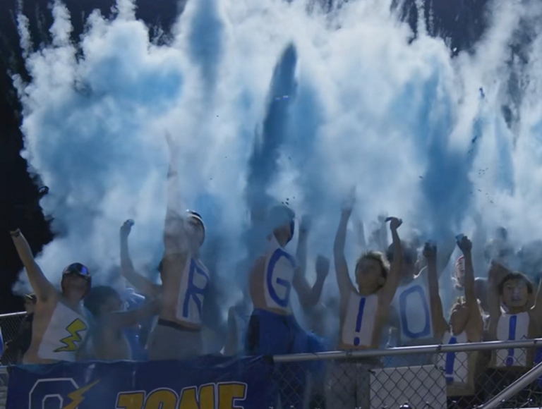 Los estudiantes de Oxford High School aplauden desde las gradas mientras una columna de polvo azul estalla sobre ellos.