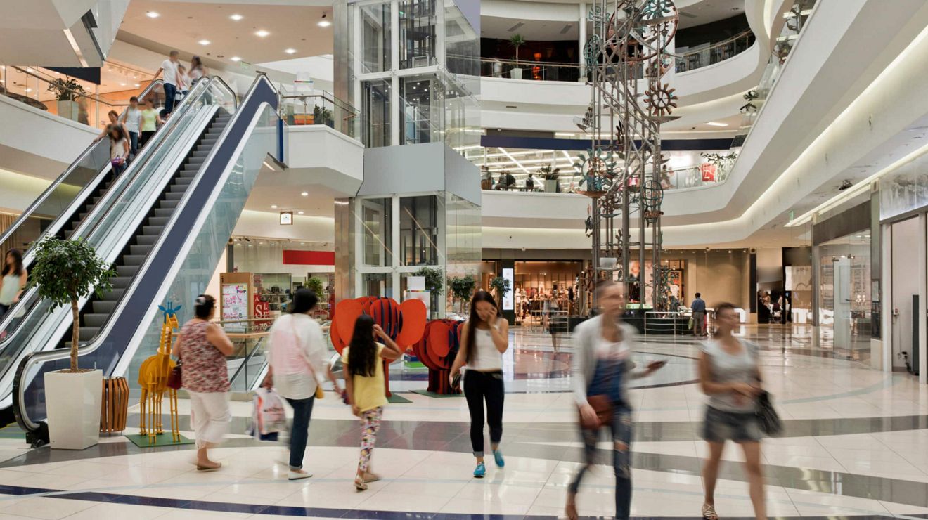 Clientes comprando en un centro comercial concurrido de varios pisos con un elevador.