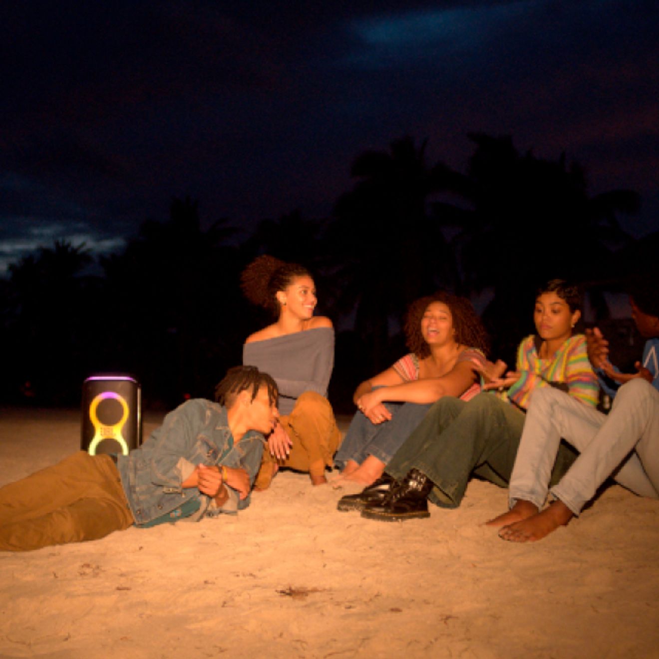Amigos en la playa por la noche escuchando música con una JBL PartyBox Club 120