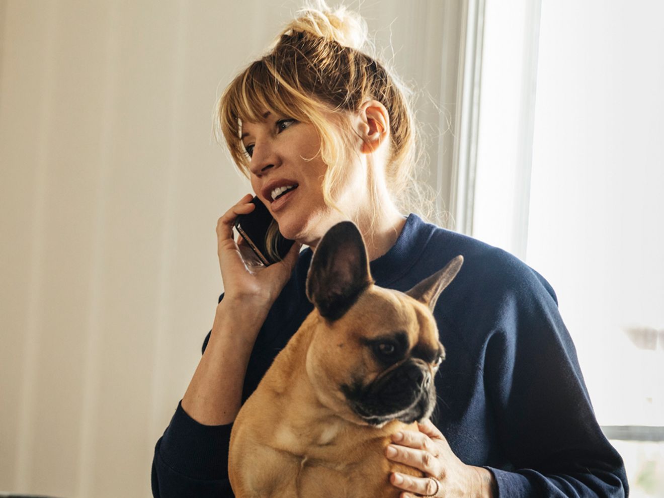 Persona realizando una llamada telefónica con un bulldog francés en su regazo.