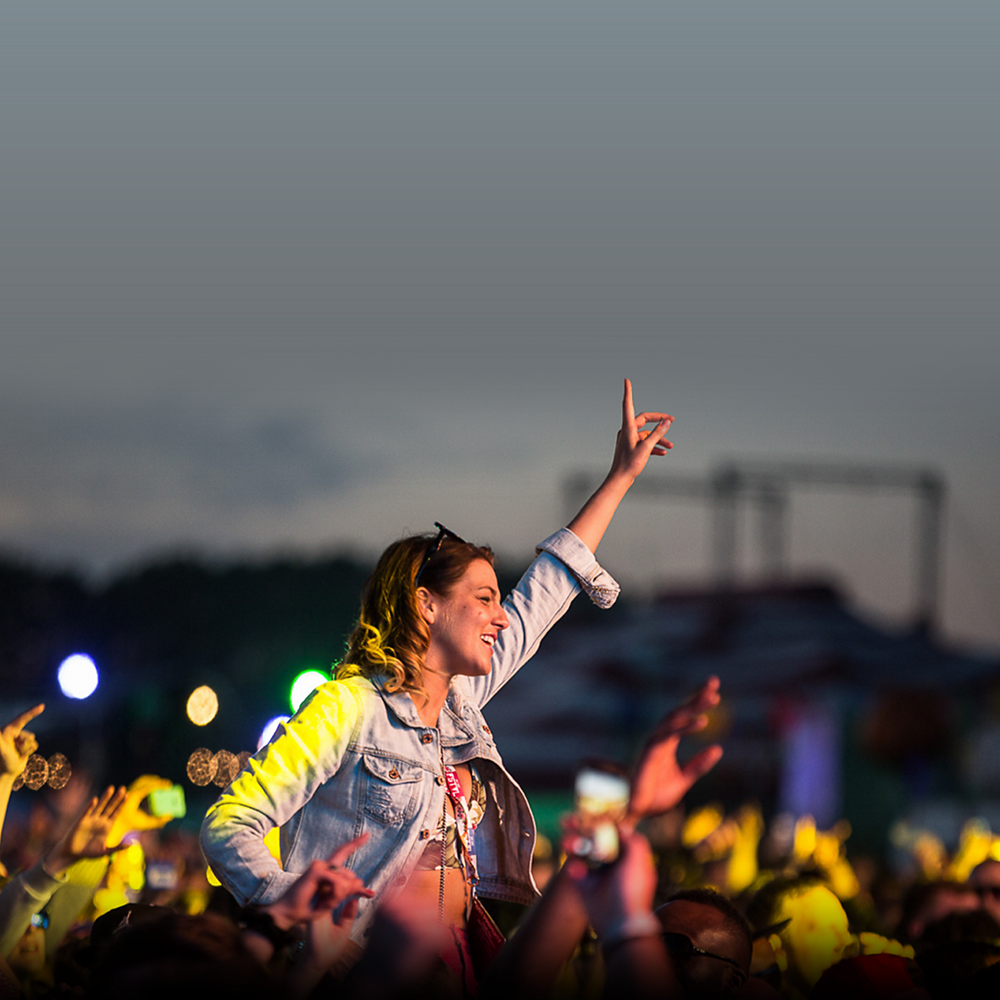 Una mujer sonriente de pie con la mano levantada en un concierto.