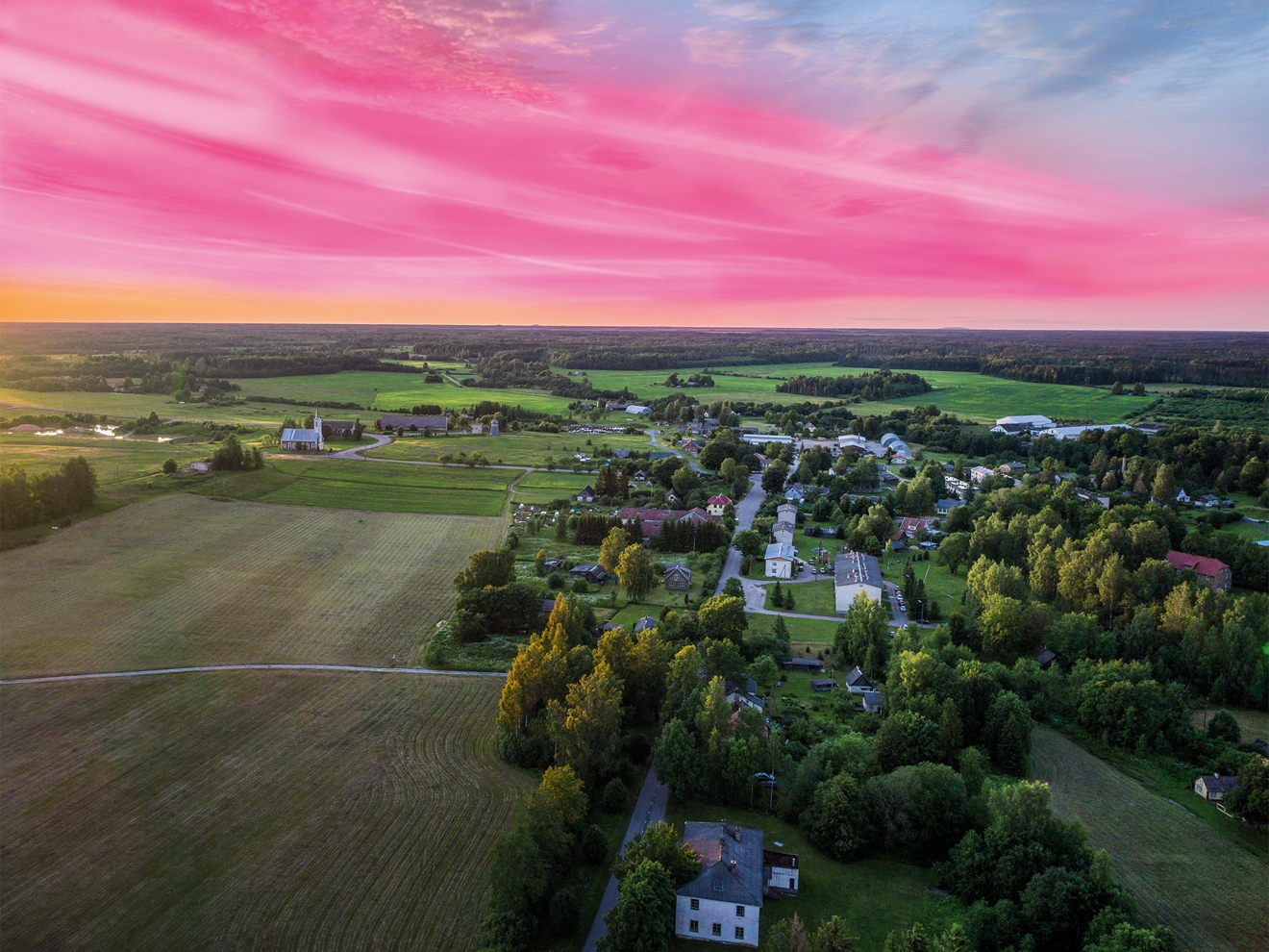 Toma aérea de un pequeño pueblo rural al atardecer con nubes magenta