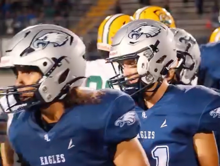 Jugadores de fútbol de South Lake, vestidos con uniformes azules y plateados, toman sus posiciones en el campo.