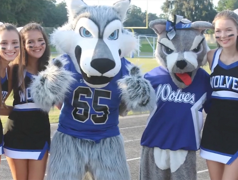 Las animadoras y mascotas de Saint Francis Catholic Academy posan para una foto en la pista del campo de fútbol.
