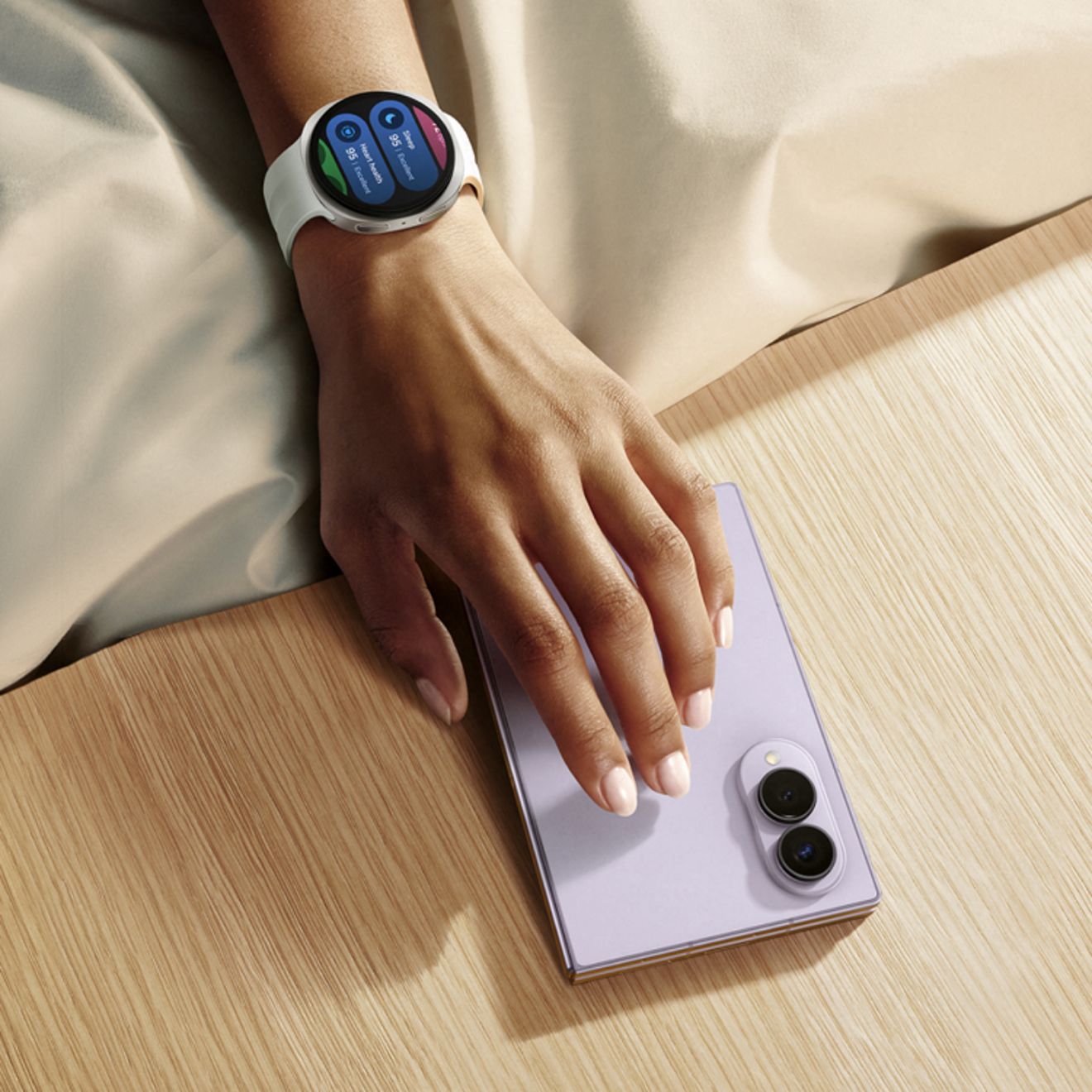 El Samsung Galaxy Z Fold8 en morado claro, se muestra cerrado sobre un escritorio junto a un Galaxy Watch con una pulsera blanca.