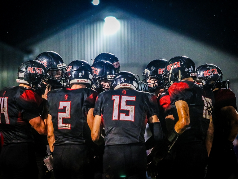 El equipo de fútbol americano de la escuela preparatoria Alden-Conger reunido durante un partido nocturno.