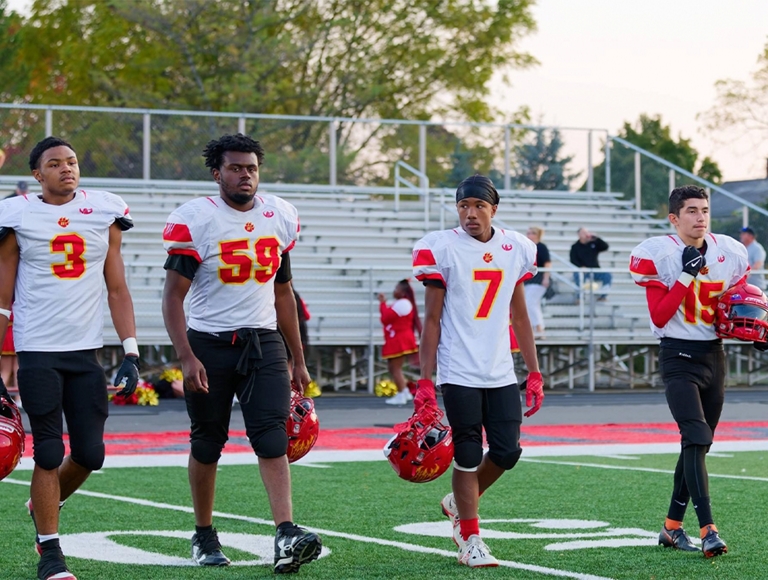Cuatro jugadores de fútbol de Bridgeport High School caminan hacia el campo sosteniendo sus cascos.