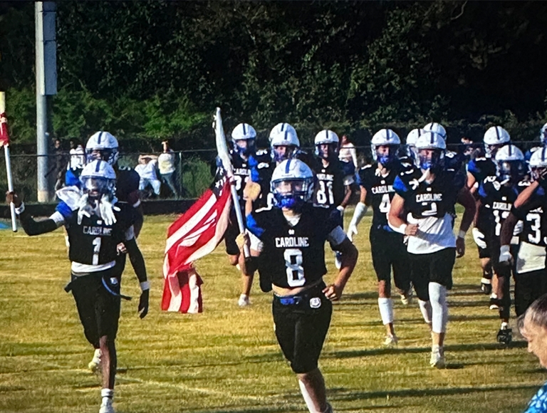 El equipo de fútbol de North Caroline corre hacia el campo con una bandera estadounidense.