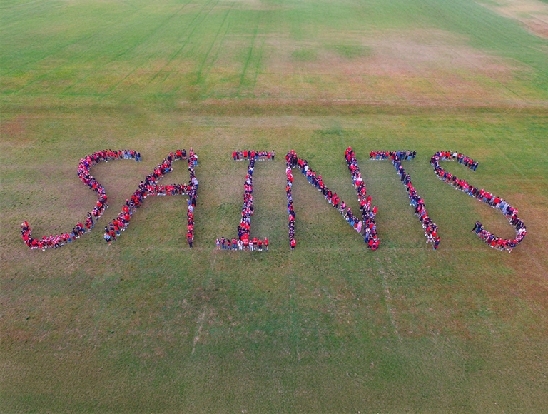 Los estudiantes de la Saint James High School deletrean la palabra "Saints" en un campo abierto.