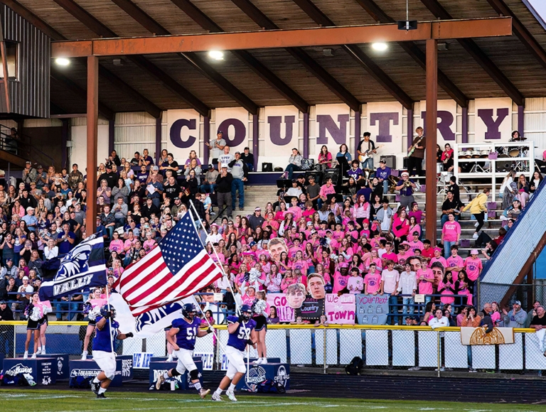 El equipo de la escuela Nooksack Valley High School corre entre una multitud entusiasta que ondea grandes banderas.