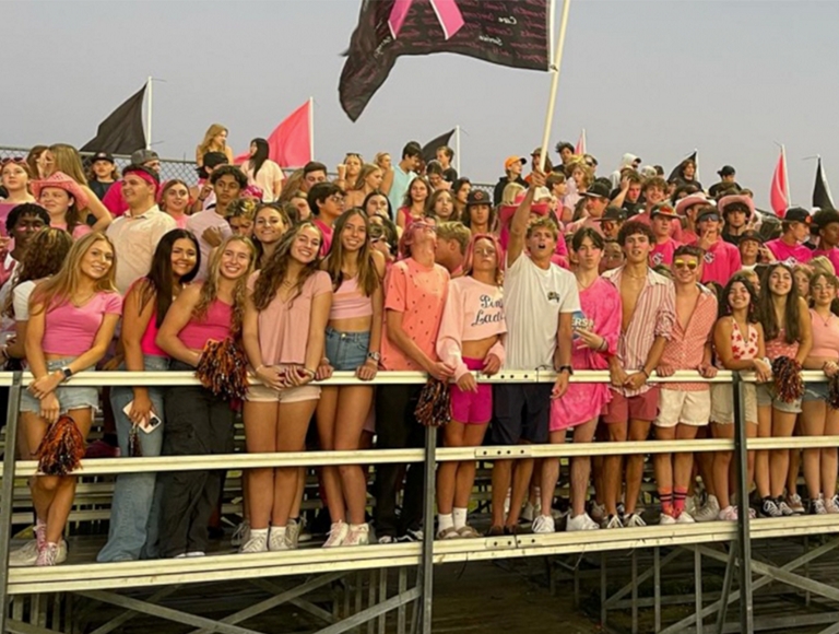 Estudiantes de Spruce Creek High School visten distintos tonos de rosa y animan desde las gradas.