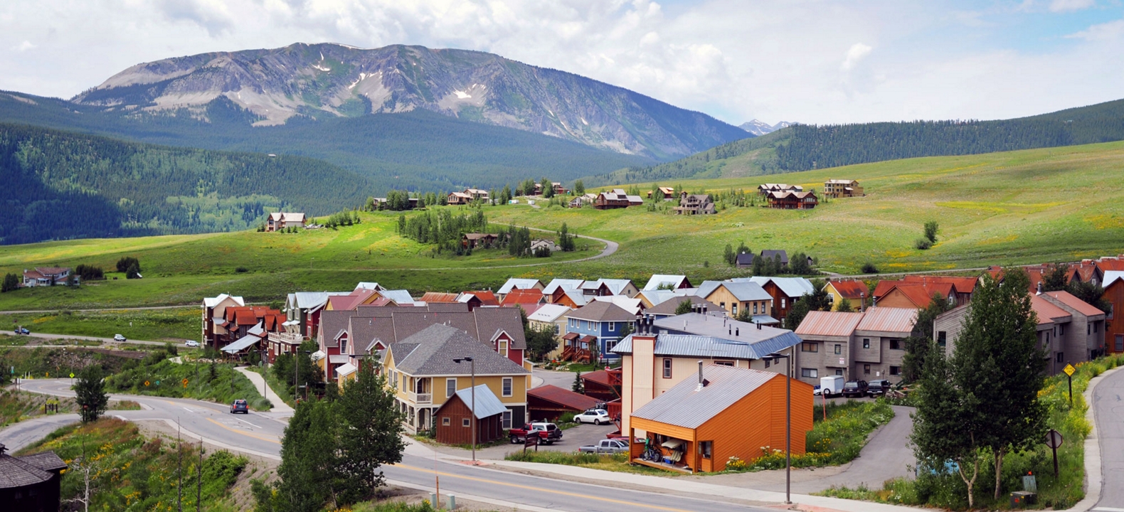 Un pueblo de casas coloridas enclavado en un valle verde, con colinas onduladas y casas dispersas al fondo.