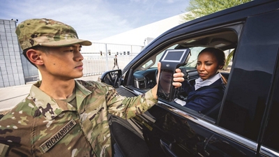 Un guardia con uniforme militar utiliza un teléfono móvil para autorizar el paso de un conductor en la puerta de acceso a las instalaciones.