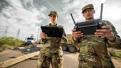 Dos personas con uniformes de camuflaje sostienen una tablet conectada y un control para drones.