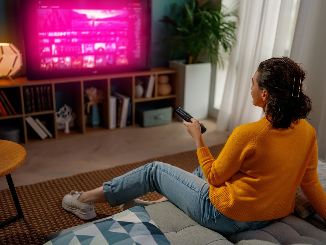 Una mujer ve televisión con el resplandor magenta de T-Mobile mientras se relaja en el sofá de su sala de estar.