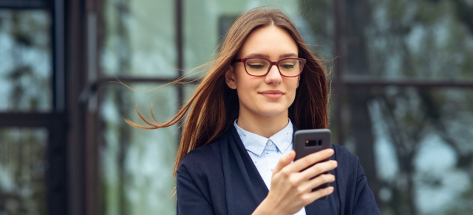 Una profesional de servicios financieros consulta su smartphone mientras camina por una calle de la ciudad