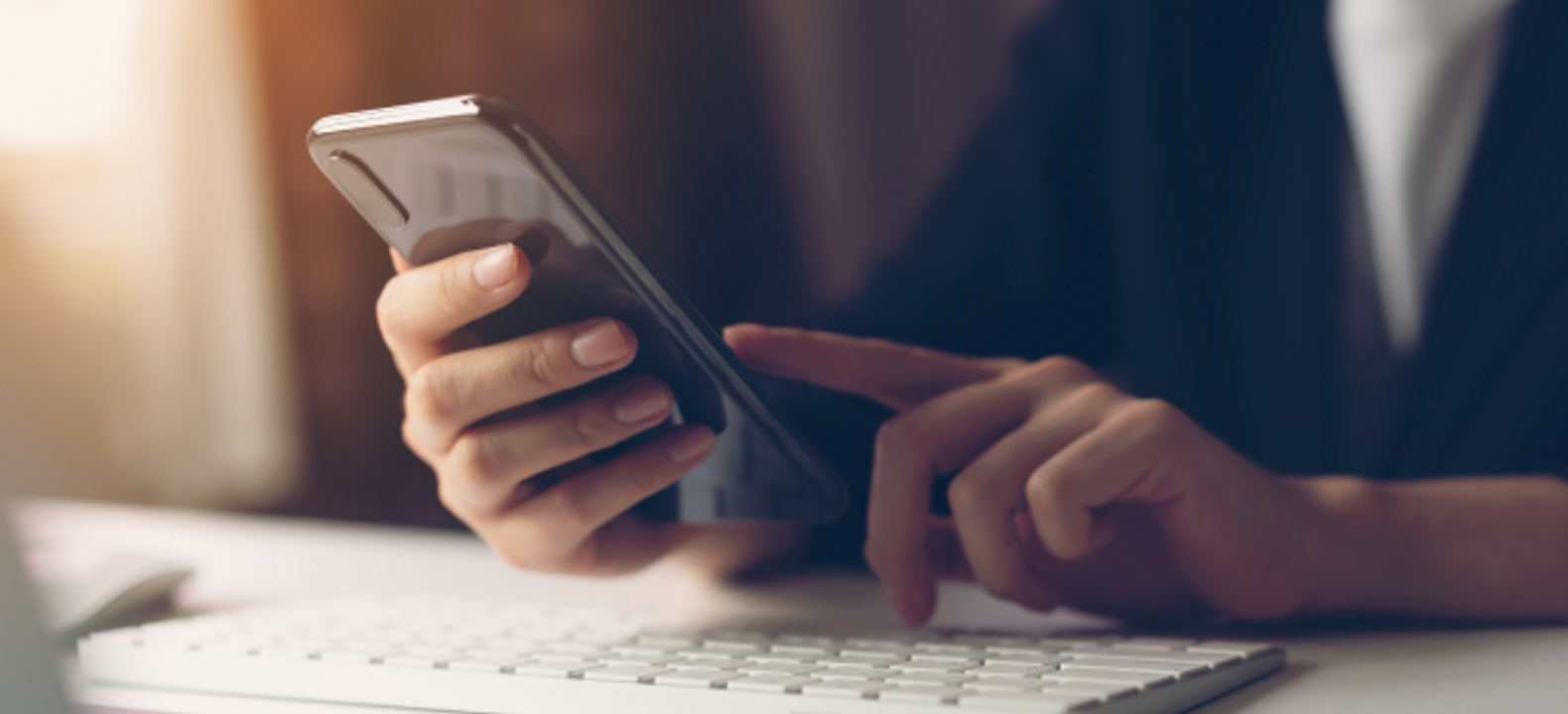 Primer plano de dos manos trabajando con un smartphone sobre un teclado de computadora