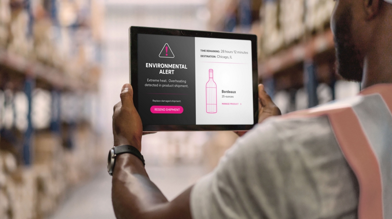 Un empleado de almacén consulta una tablet que muestra una advertencia sobre el sobrecalentamiento de un producto vinícola despachado.