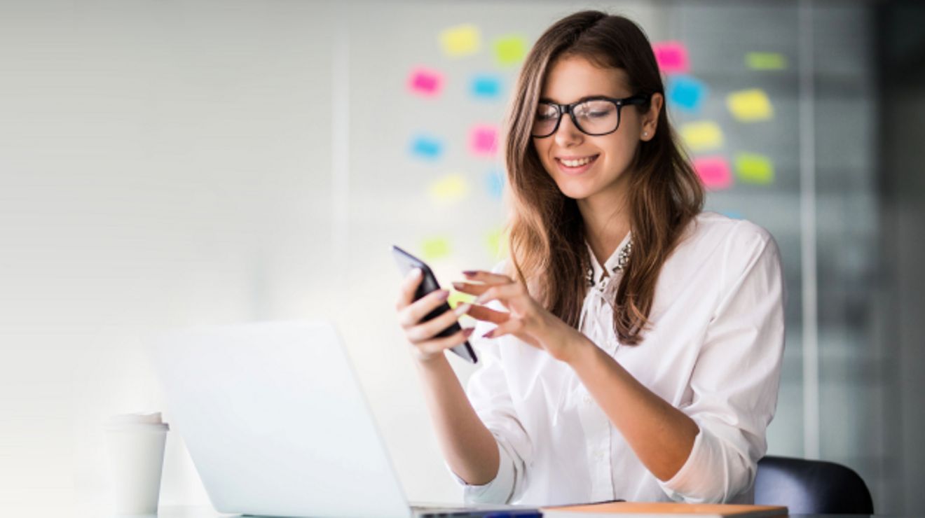 Una profesional sonriente con su smartphone en un entorno de oficina moderno.